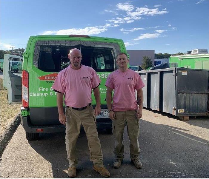 SERVPRO team members, donned in pink shirts, stand by SERVPRO vehicles
