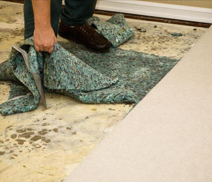 A person pulling up carpet and padding 