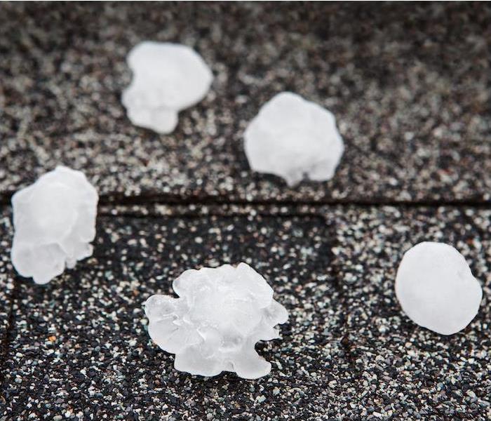 large pieces of hail melting on dark roof shingles