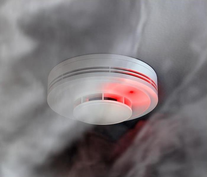 white fire alarm hanging on ceiling flashing red from rising smoke